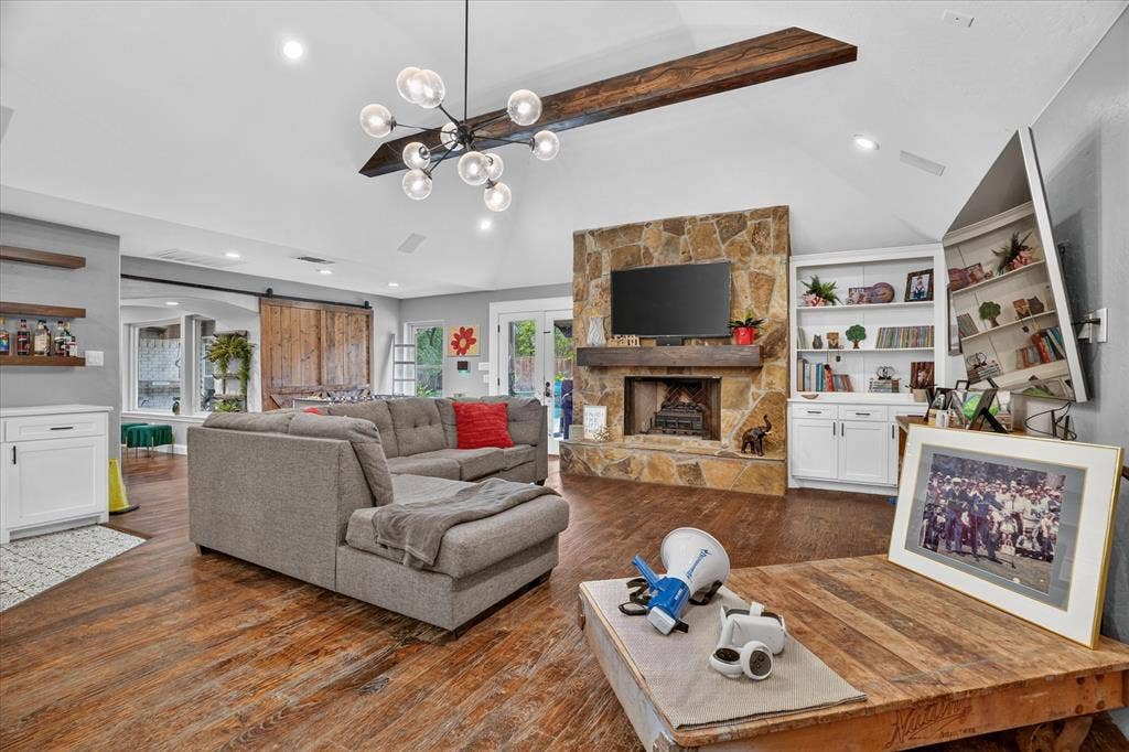 7016 Battle Creek Road, Fort Worth, TX 76116 Vaulted ceilings featuring a chandelier, stone-clad fireplace, wood-finish flooring, built-in shelving, and barn door access