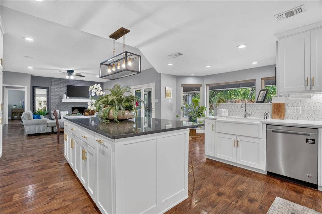 7016 Battle Creek Road, Fort Worth, TX 76116 Spacious kitchen featuring an expansive island with a dark countertop, white shaker-style cabinetry with gold-tone hardware, wood-finish flooring, a white apron-front sink, and stainless steel appliances