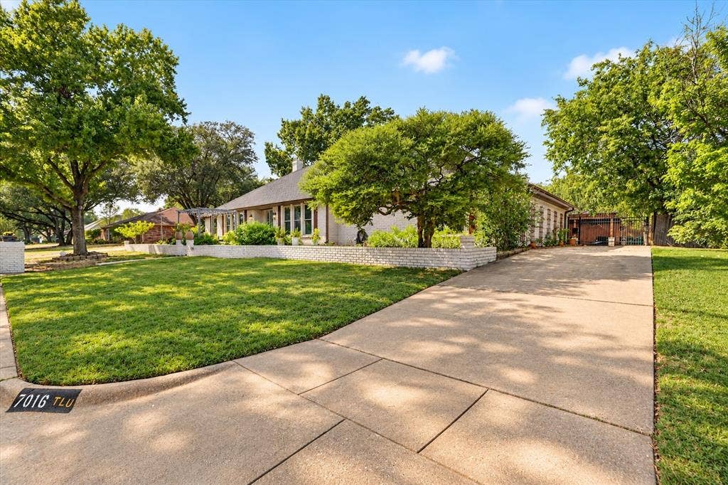 7016 Battle Creek Road, Fort Worth, TX 76116 Expansive front lawn with mature trees, a curved concrete driveway, and a white brick planter wall