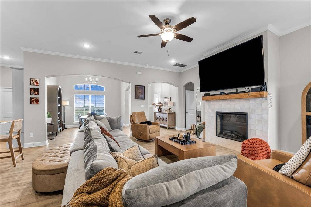 Spacious living area featuring wood-finish flooring, a tiled fireplace with wood mantel, and arched doorways