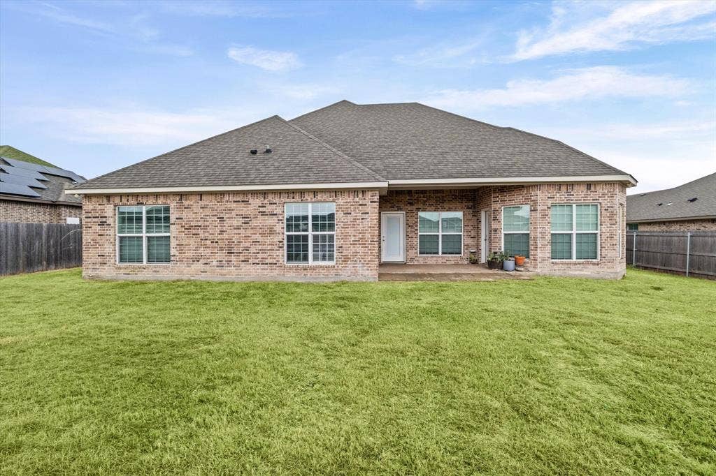 Expansive grassy yard with a brick exterior, covered patio, and multiple windows