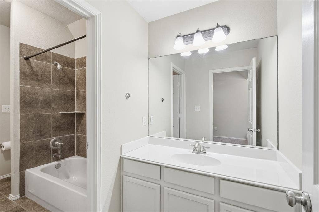 750 Village Green Drive, DeSoto, TX 75115 Full vanity mirror, white flat-panel cabinetry, white countertop, integrated sink, and tub-shower combination with tiled surround