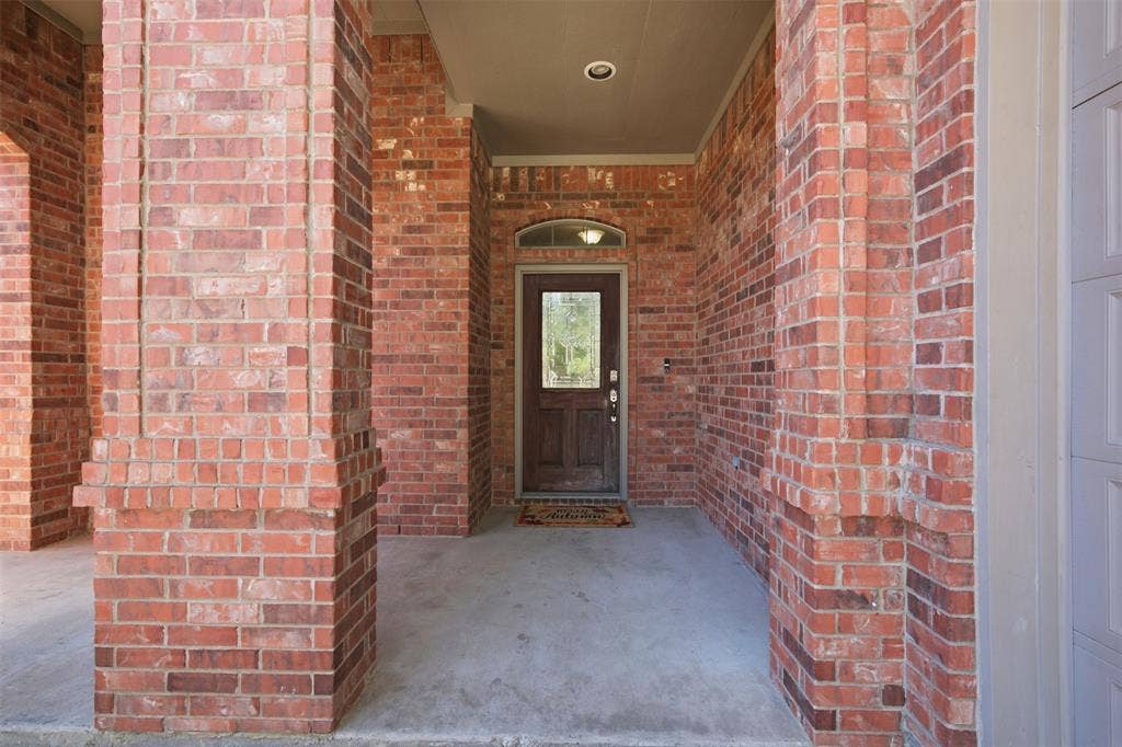 750 Village Green Drive, DeSoto, TX 75115 Brick exterior with decorative brick columns, covered concrete entry, recessed lighting, and a wood-panel entry door with an arched transom window