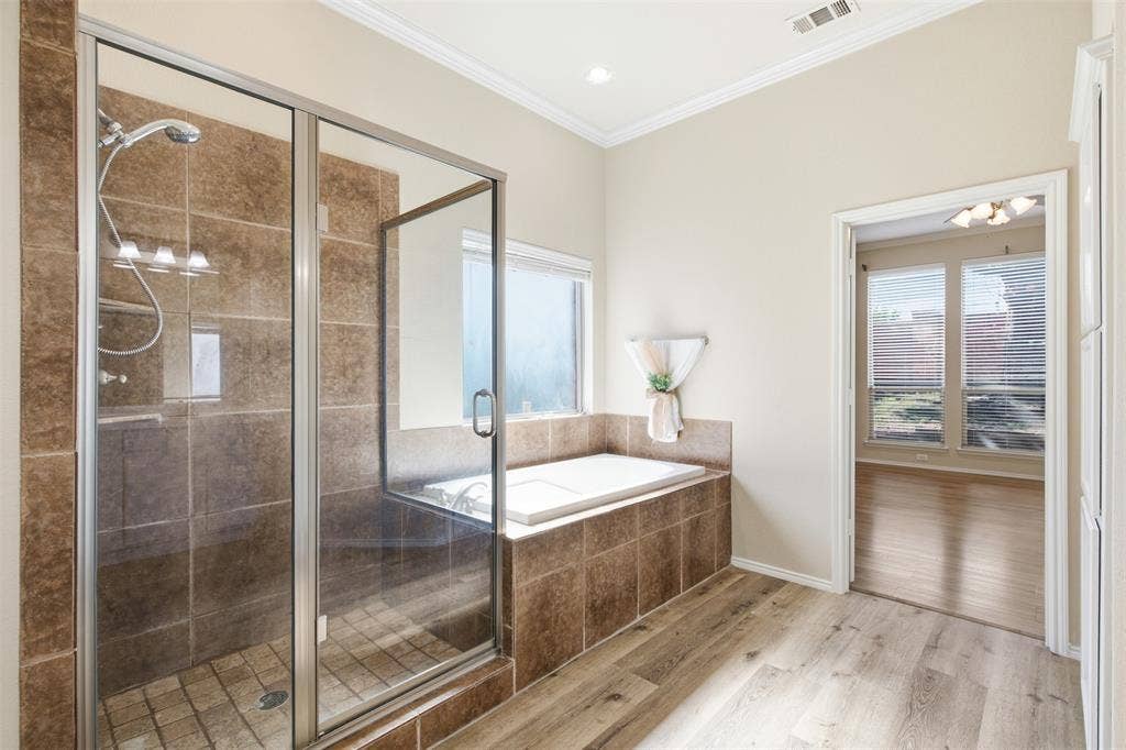 750 Village Green Drive, DeSoto, TX 75115 Glass-enclosed shower with tile surround, separate built-in soaking tub, wood-finish flooring, and crown molding