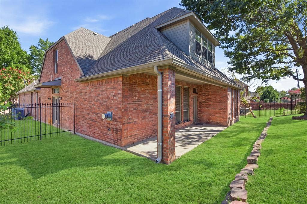 750 Village Green Drive, DeSoto, TX 75115 Brick exterior with a covered patio, dormer window, and asphalt shingle roof. Green enhancement to lawn.