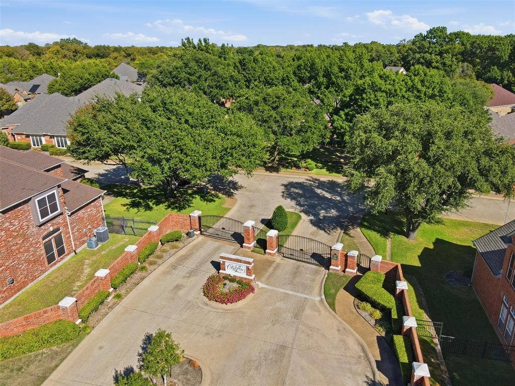 750 Village Green Drive, DeSoto, TX 75115 Gated community entrance with brick pillars, wrought iron gates, and a landscaped central island