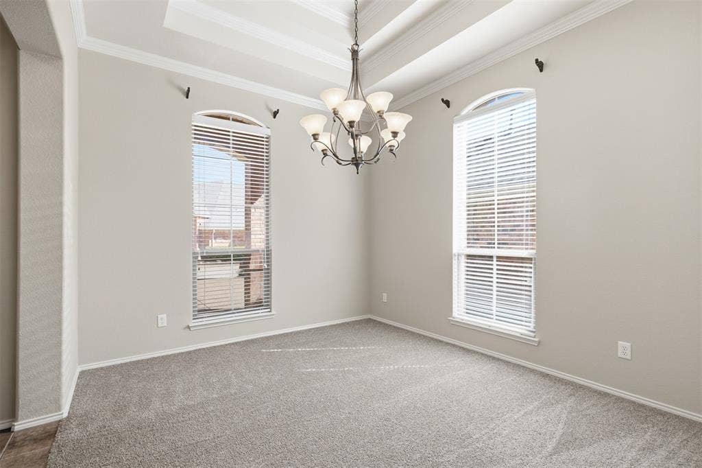 750 Village Green Drive, DeSoto, TX 75115 Tray ceiling with crown molding, chandelier lighting, two arched windows with blinds, and carpet flooring
