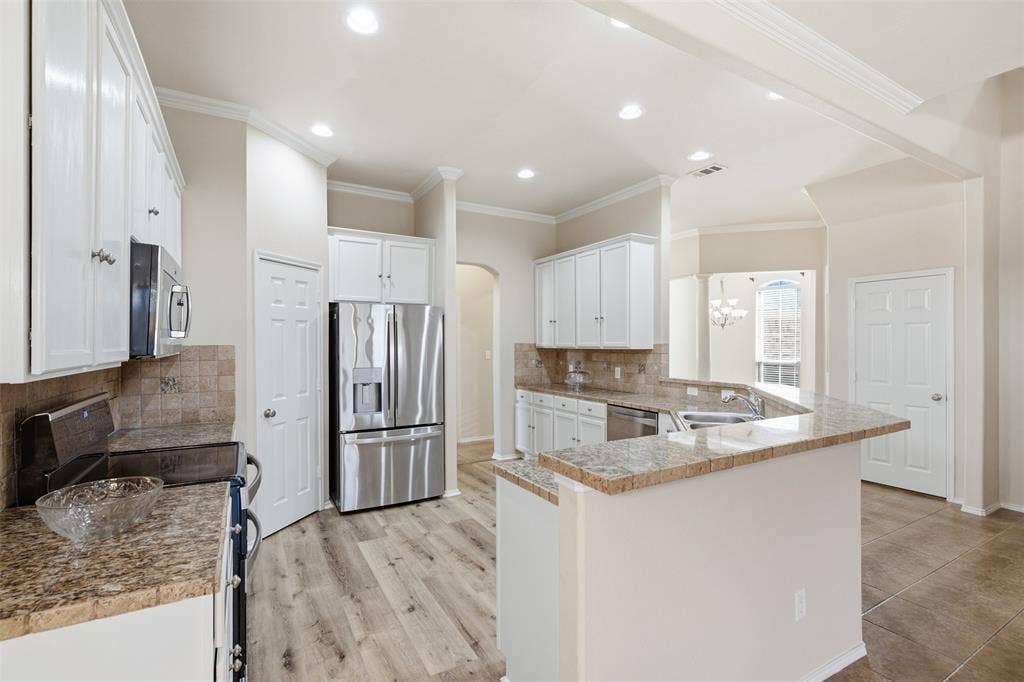 750 Village Green Drive, DeSoto, TX 75115 Kitchen featuring white cabinetry, granite countertops, stainless steel appliances, wood-finish flooring, and crown molding
