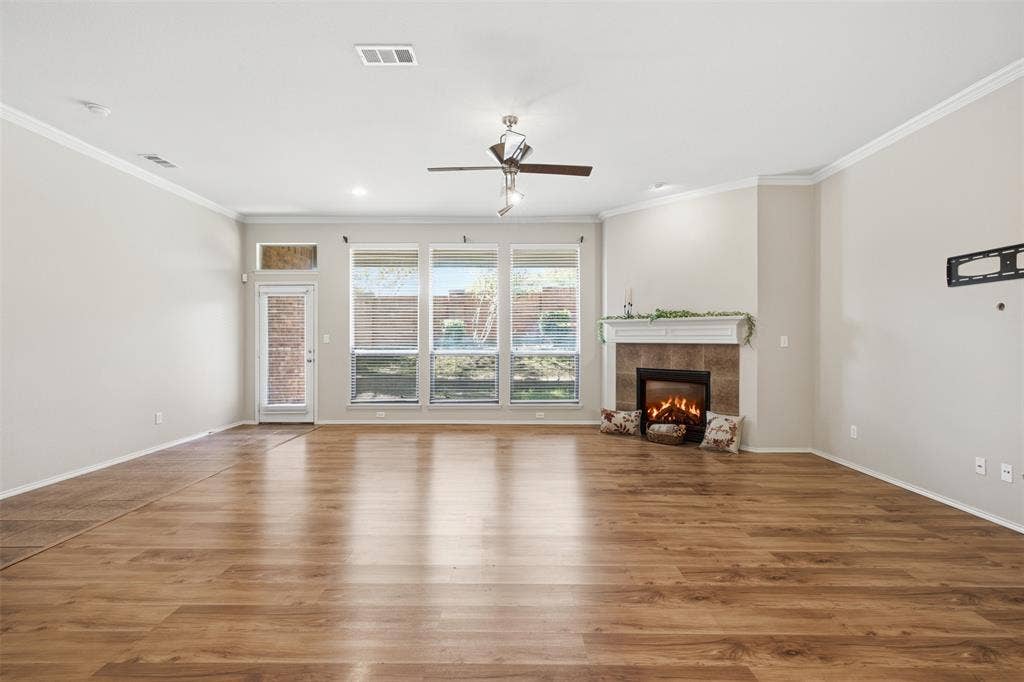 750 Village Green Drive, DeSoto, TX 75115 Wood-finish flooring throughout, a tiled fireplace with a white mantel, multiple large windows, a glass-paned door, and a ceiling fan with integrated lighting