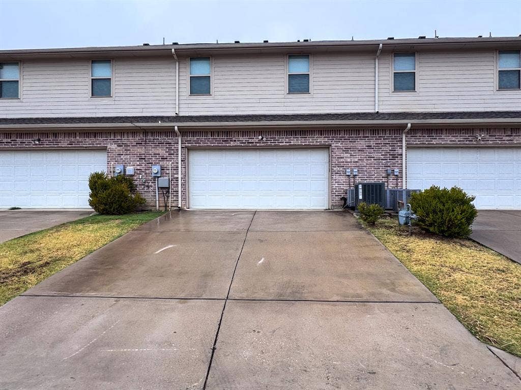 4814 Empire Way, Irving, TX 75038 Brick and siding exterior featuring white garage doors, upper-level windows, and concrete driveways