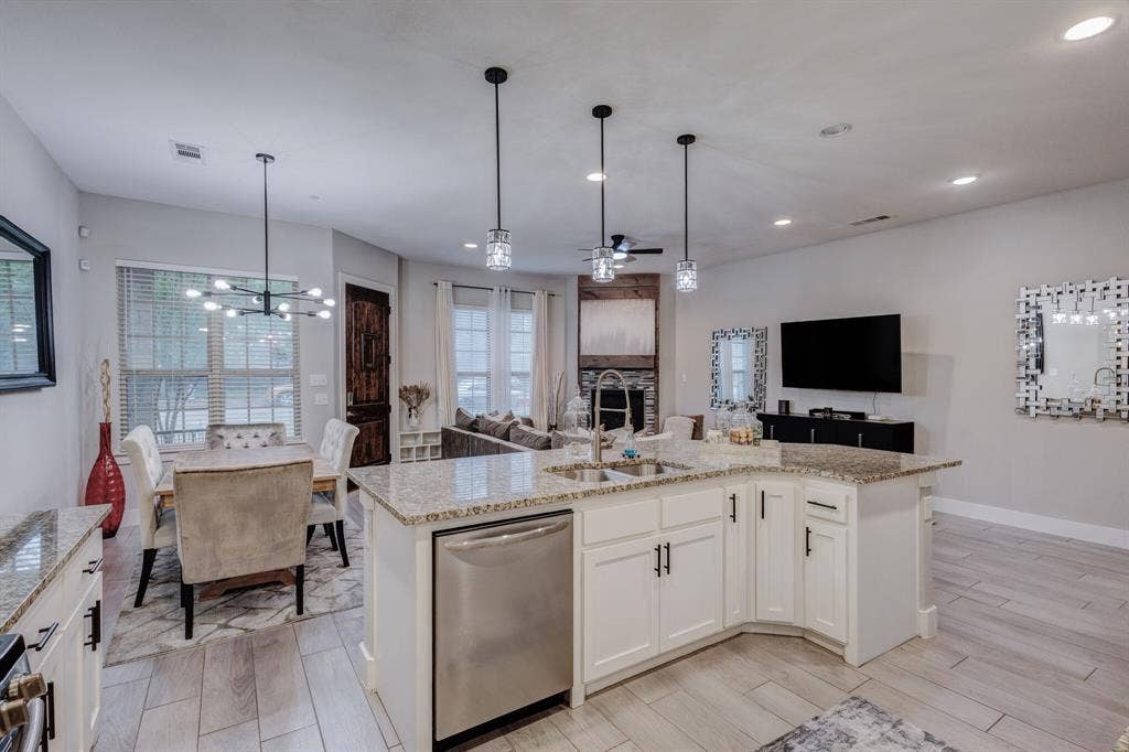 4814 Empire Way, Irving, TX 75038 Kitchen island with white cabinetry and granite countertops, stainless steel dishwasher, pendant lighting fixtures, and light-toned wood-finish flooring