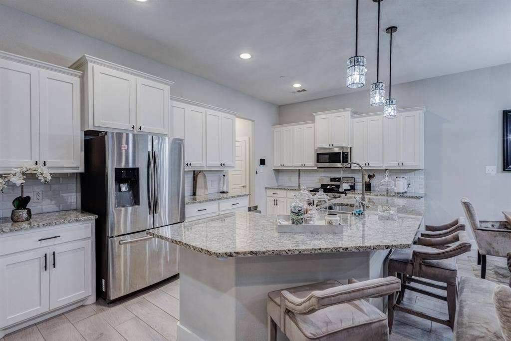 4814 Empire Way, Irving, TX 75038 White shaker cabinetry, stainless steel appliances, speckled stone countertops, tile backsplash, and decorative pendant lighting