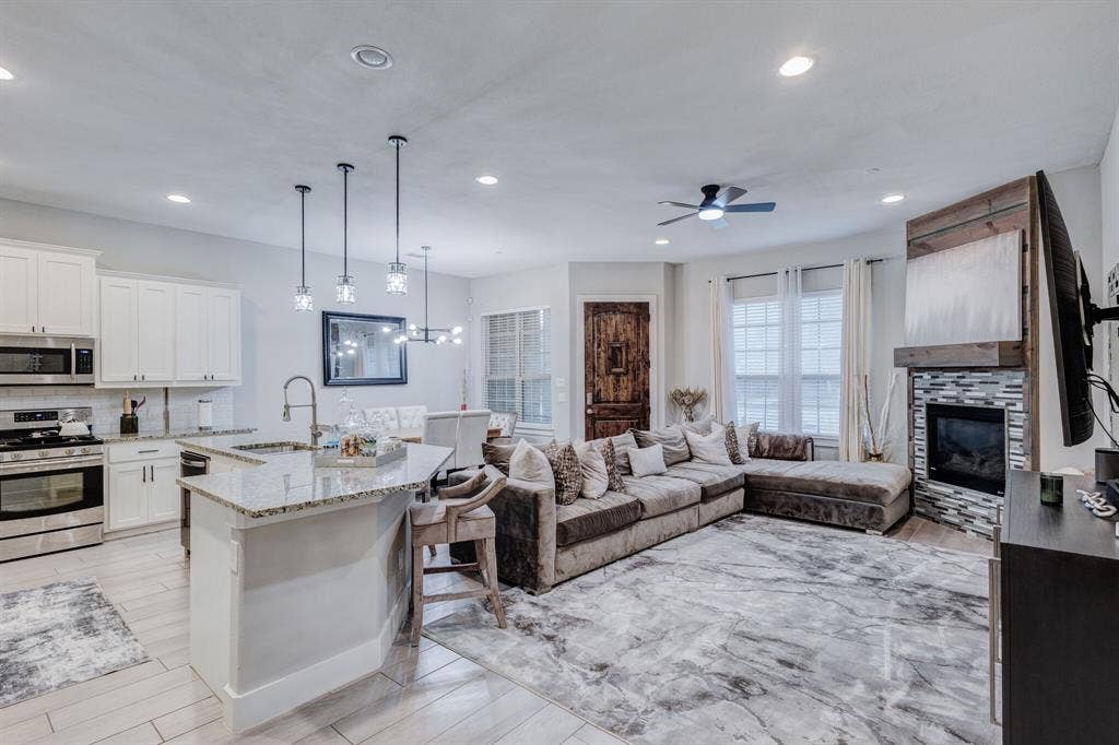 4814 Empire Way, Irving, TX 75038 Open-concept living area featuring wood-finish flooring, a kitchen island with stone countertop, stainless steel appliances, and a tiled fireplace