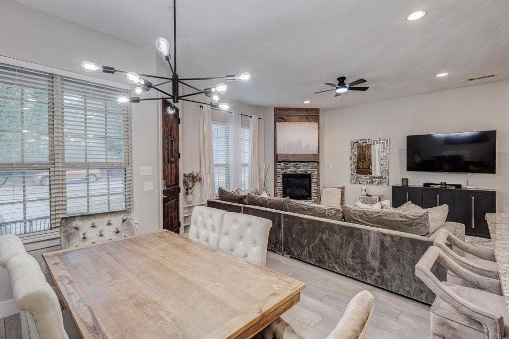 4814 Empire Way, Irving, TX 75038 Open-concept living space with light wood-finish flooring, a contemporary chandelier, recessed lighting, and a built-in fireplace with a stone surround and wood mantle
