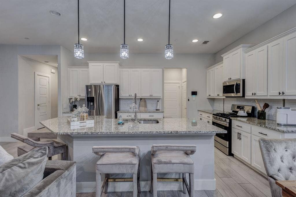 4814 Empire Way, Irving, TX 75038 Kitchen featuring a large island with stone countertop, white shaker cabinetry, stainless steel appliances, and pendant lighting