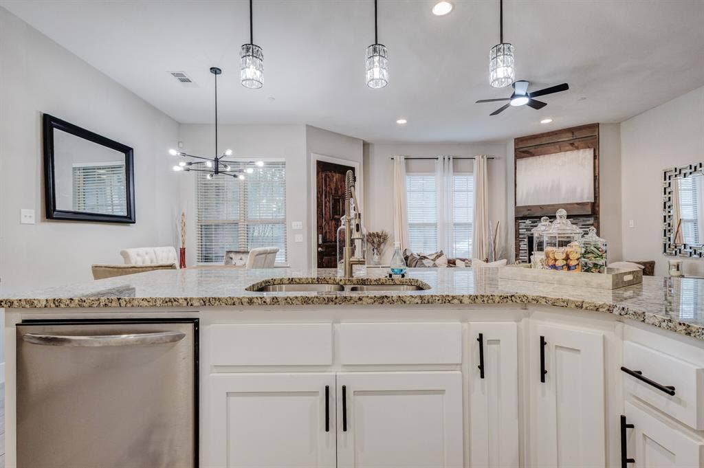4814 Empire Way, Irving, TX 75038 Kitchen island featuring a stainless steel sink with a high-arch faucet, granite-style countertop, and white cabinetry with matte black hardware
