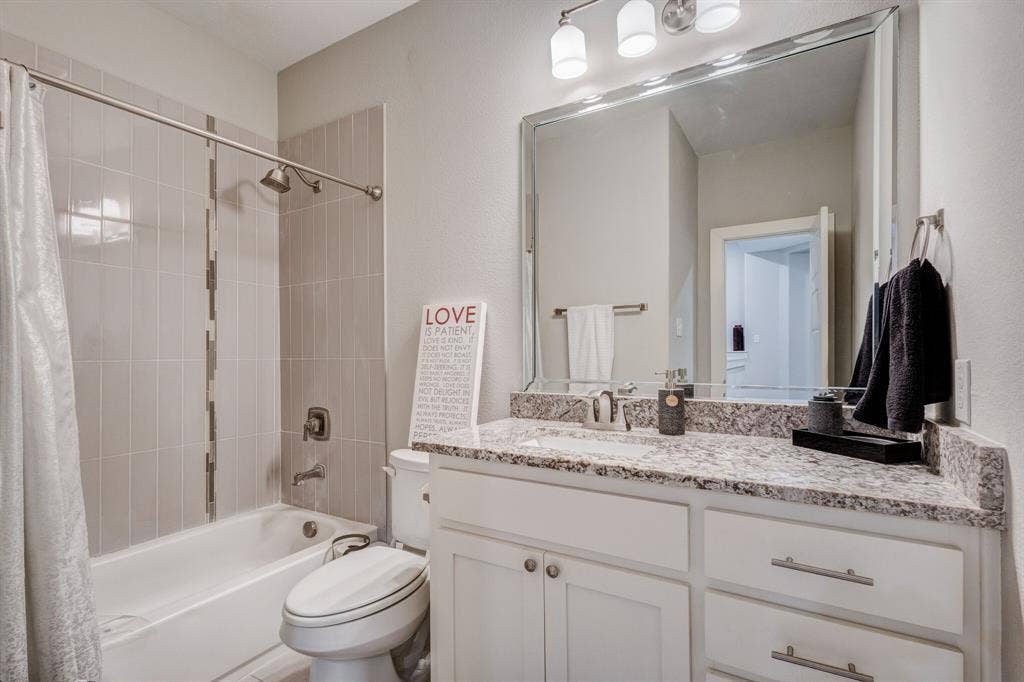 4814 Empire Way, Irving, TX 75038 Bathtub with vertical tile surround, vanity with granite countertop, undermount sink, white cabinetry with silver hardware, and a large wall-mounted mirror