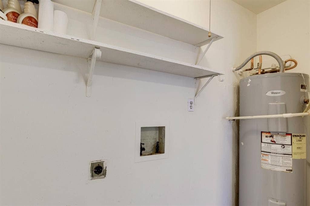 Wall-mounted shelving, recessed laundry hookups, and a dedicated electrical outlet, accompanied by a tank-style water heater