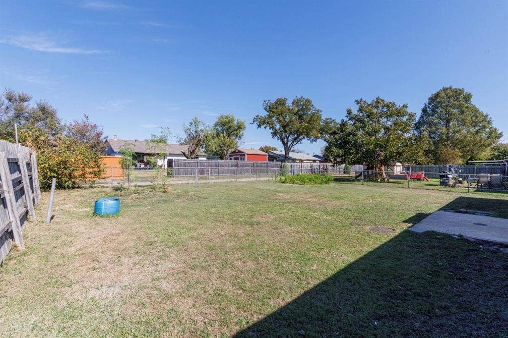 Expansive backyard featuring a large grass lawn, mature trees, concrete patio, and perimeter wood fencing