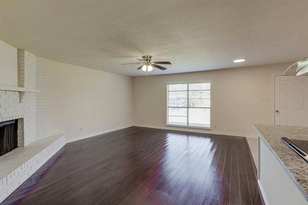 Wood-finish flooring, white painted brick fireplace with raised hearth, recessed lighting, and ceiling fan with integrated light fixture