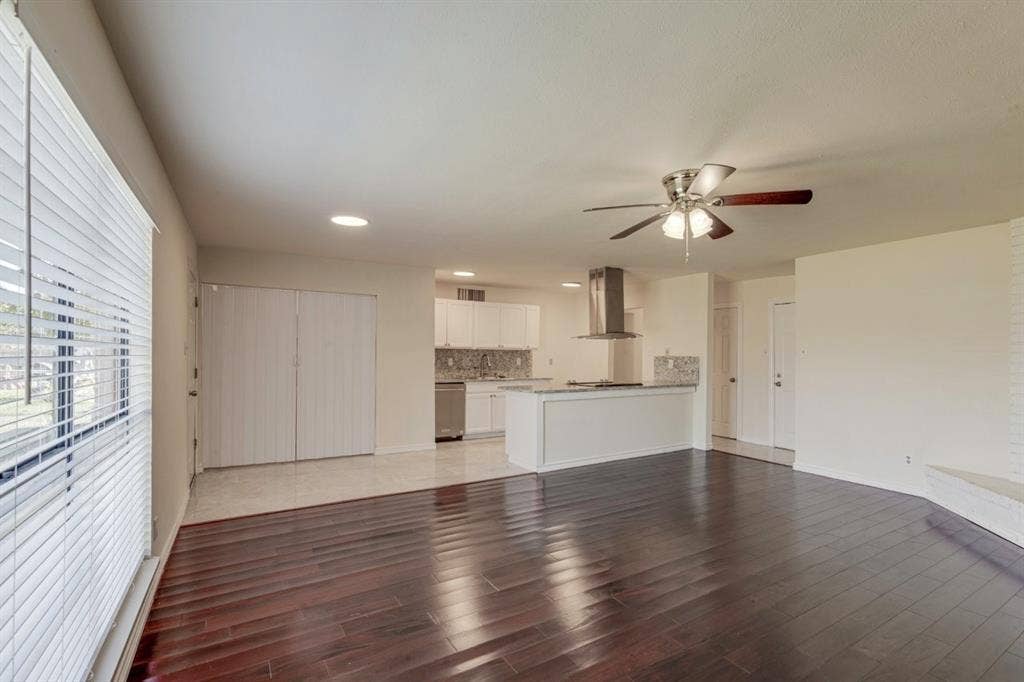 Open-concept room featuring dark wood-finish flooring, white cabinetry, a stainless steel range hood, stone-finish backsplash, and a ceiling fan