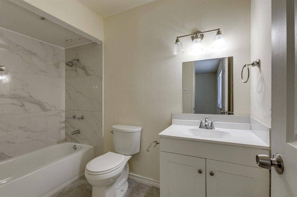 Full bathroom featuring a tub-shower combination with floor-to-ceiling stone-pattern tile, a white vanity with an integrated basin, a three-light vanity fixture, and a rectangular mirror