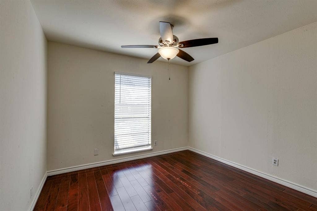 Interior room featuring wood-finish flooring, a neutral wall palette, a single window with horizontal blinds, and a central ceiling fan with an integrated light fixture