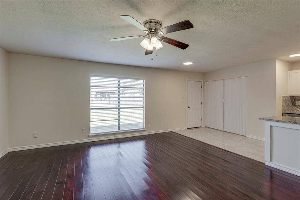 Interior space featuring dark wood-finish flooring, a ceiling fan with integrated lighting, a large window with horizontal blinds, and tile flooring near the built-in storage closets