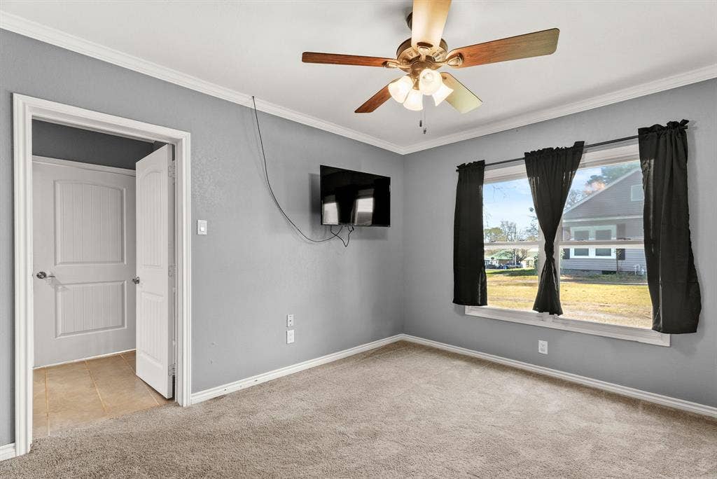 605 Dallas Street, Winona, TX 75792 Light grey wall paint, crown molding, ceiling fan with light fixture, window with white trim, and carpeted flooring