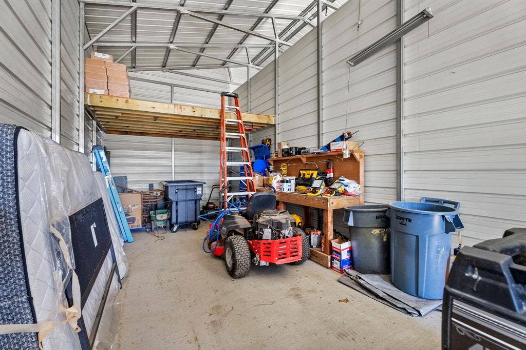 605 Dallas Street, Winona, TX 75792 Concrete floor, metal siding, exposed metal roof trusses, built-in wooden workbench, and overhead storage platform
