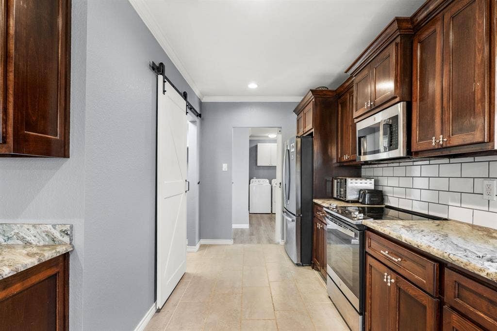 605 Dallas Street, Winona, TX 75792 Galley kitchen featuring wood cabinetry, stone countertops, stainless steel appliances, and a subway tile backsplash