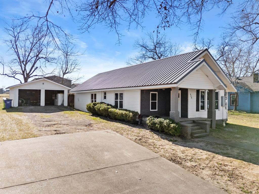 605 Dallas Street, Winona, TX 75792 White siding exterior with a dark metal roof, concrete driveway, and a detached two-car garage
