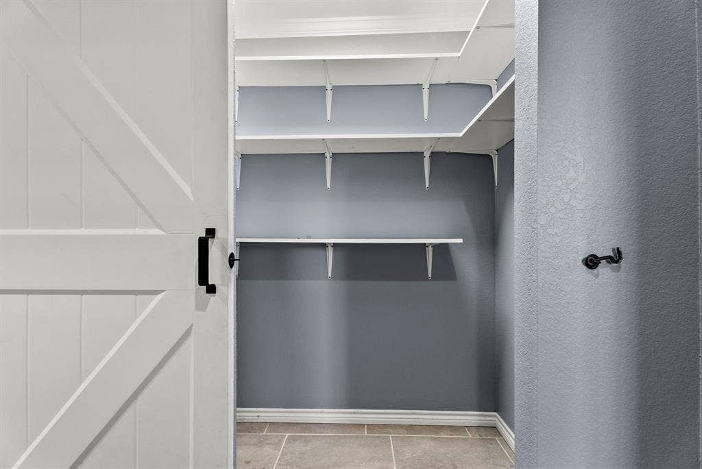 605 Dallas Street, Winona, TX 75792 Sliding barn door with matte black hardware, gray wall tones, tile flooring, white shelving system, and white trim