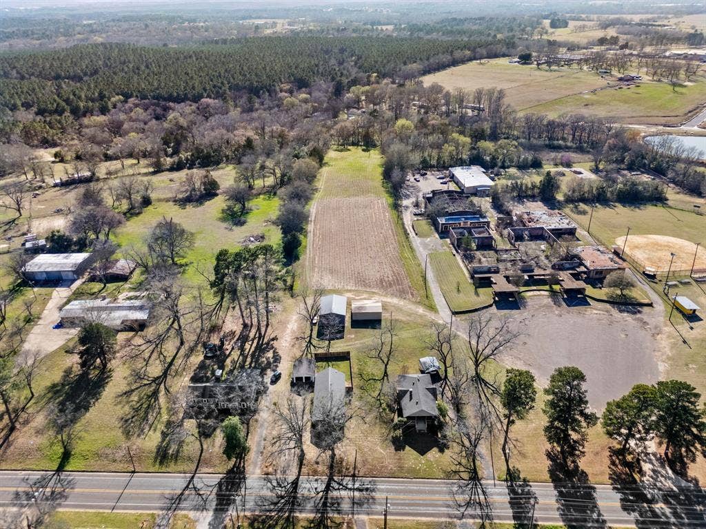 605 Dallas Street, Winona, TX 75792 Expansive rural landscape featuring a cultivated field, mature trees, and a distant forested area