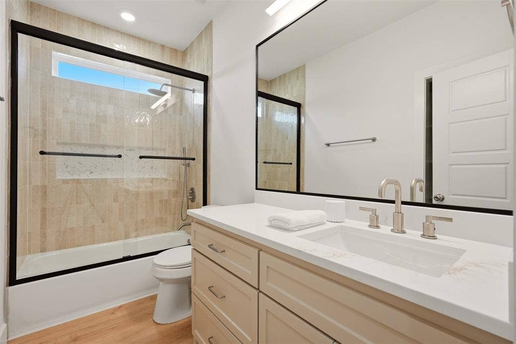 1601 Birdell Street, Fort Worth, TX 76105 Floating vanity with a rectangular undermount sink, brushed nickel faucet, large frameless mirror, and a shower-tub combination with tile surround