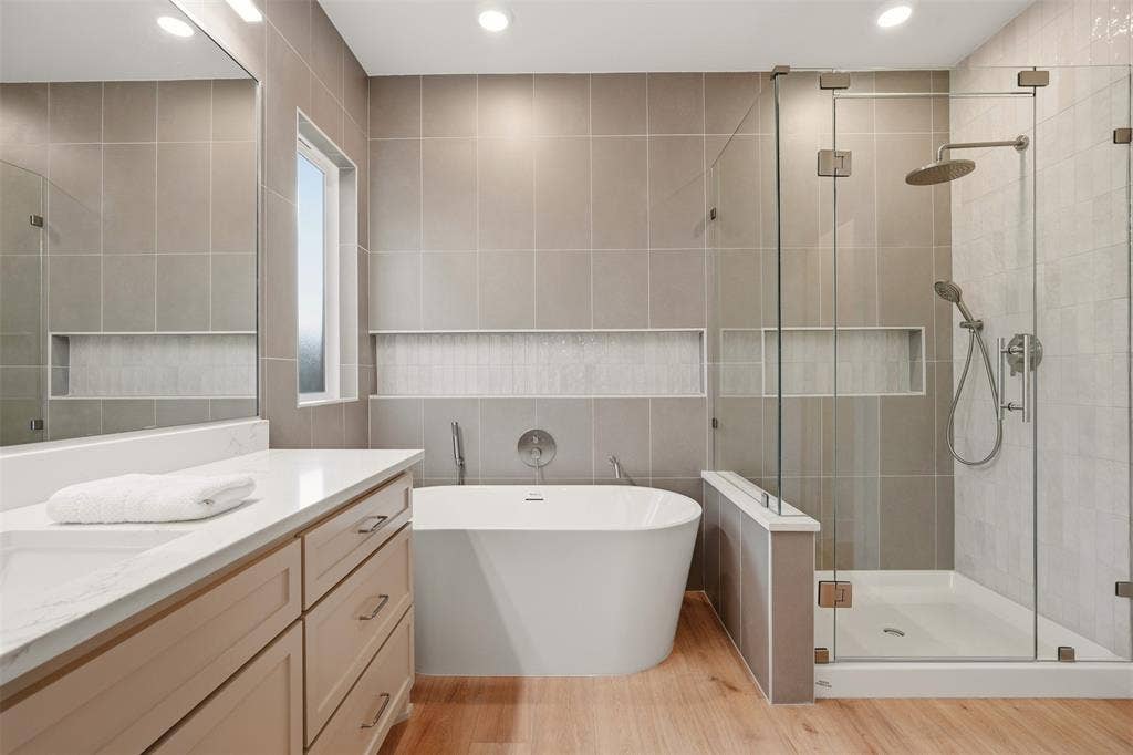 1601 Birdell Street, Fort Worth, TX 76105 Walk-in shower with clear glass enclosure and rainfall showerhead, freestanding soaking tub, wood-finish flooring, vanity with light-colored countertop and drawers, and recessed wall niches