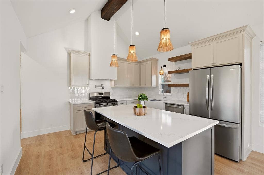 1601 Birdell Street, Fort Worth, TX 76105 Vaulted ceiling with exposed wood beam, kitchen island with solid surface countertop, wood-finish flooring, stainless steel appliances, and white tile backsplash