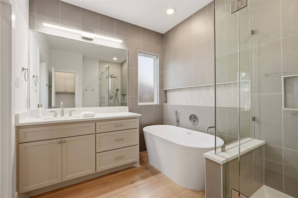 1601 Birdell Street, Fort Worth, TX 76105 Freestanding soaking tub, frameless glass shower enclosure with built-in bench, light wood-finish flooring, vanity with light-colored countertop, and recessed lighting