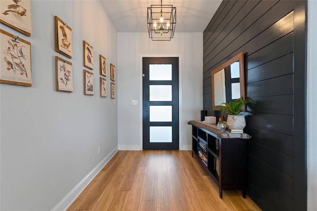 149 Water View Lane, Robinson, TX 76706 Wood-finish flooring, accent wall with horizontal paneling, modern entry door with frosted glass panels, and a ceiling-mounted light fixture