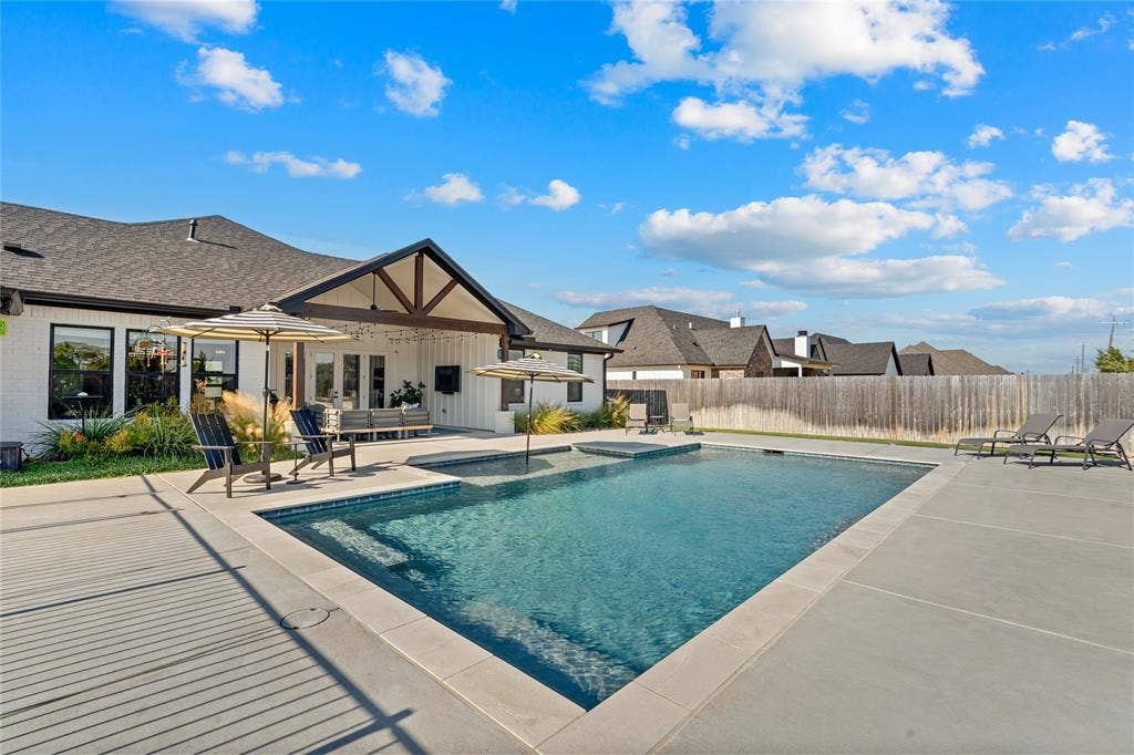 149 Water View Lane, Robinson, TX 76706 Contemporary home exterior with a dark shingle roof, a covered patio featuring exposed timber beams, a rectangular swimming pool, an integrated spa, and an expansive concrete pool deck