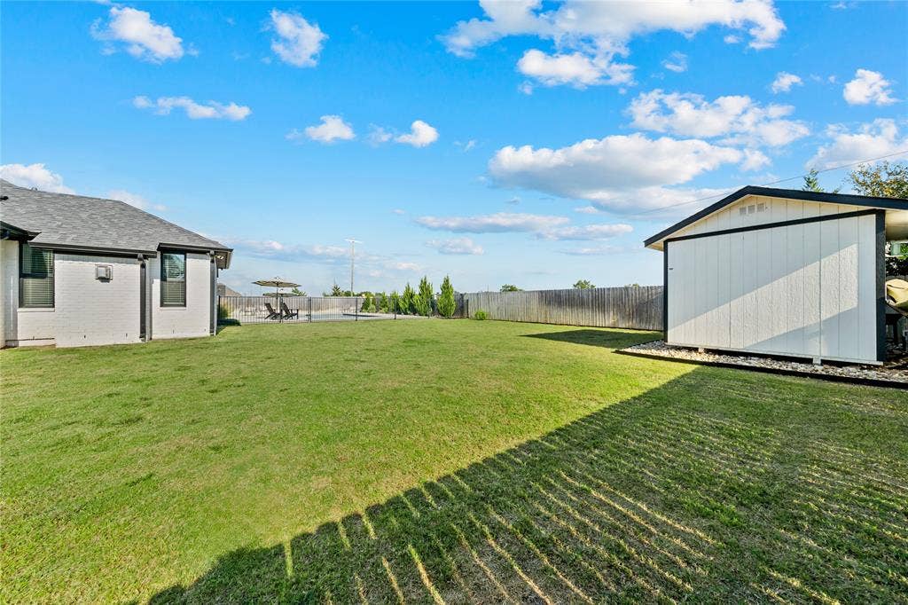 149 Water View Lane, Robinson, TX 76706 Expansive green space featuring a white siding shed, a wood fence, and a white stucco exterior building
