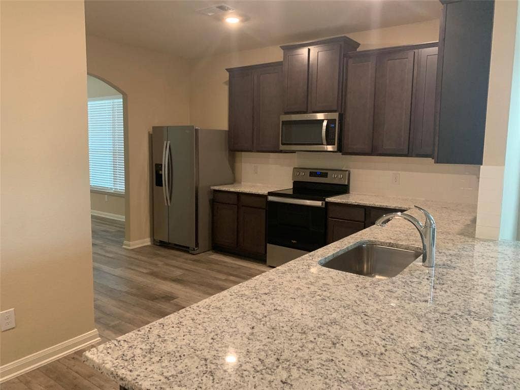 Granite countertops, stainless steel appliances, dark wood cabinetry, and wood-finish flooring
