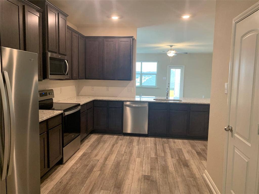 Kitchen featuring wood-finish flooring, dark wood cabinetry, light speckled countertops, and stainless steel appliances