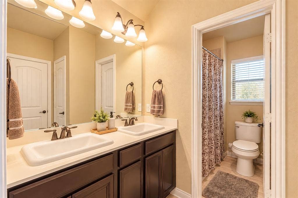 1704 Keswick Drive, McKinney, TX 75071 Double vanity with dark wood-finish cabinetry, dual undermount sinks, and bronze-finish faucets