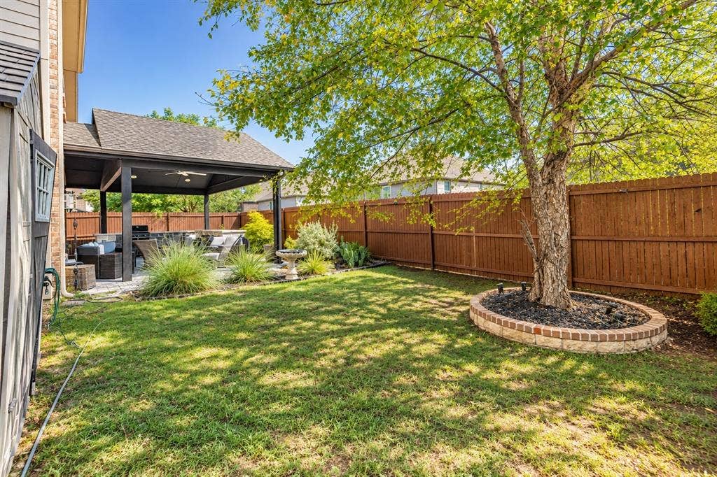 1704 Keswick Drive, McKinney, TX 75071 Expansive backyard featuring a manicured lawn, a covered patio with a ceiling fan, and mature trees
