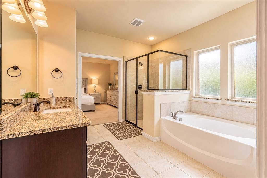 1704 Keswick Drive, McKinney, TX 75071 Bathroom featuring a spacious soaking tub, glass-enclosed shower, dual vanity with granite-style countertop, and tile flooring
