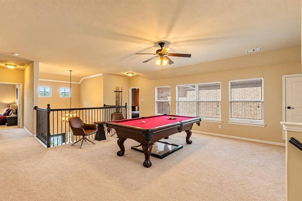 1704 Keswick Drive, McKinney, TX 75071 Spacious loft area featuring carpet flooring, multiple windows with blinds, a ceiling fan, and black metal railing overlooking the lower level