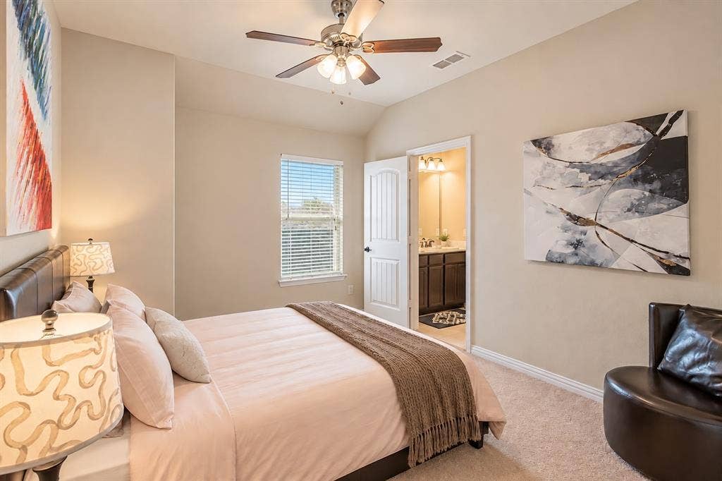 1704 Keswick Drive, McKinney, TX 75071 Carpeted bedroom with a built-in ceiling fan, single window with blinds, and an attached three-piece bathroom featuring a dark wood-finish vanity with a single sink