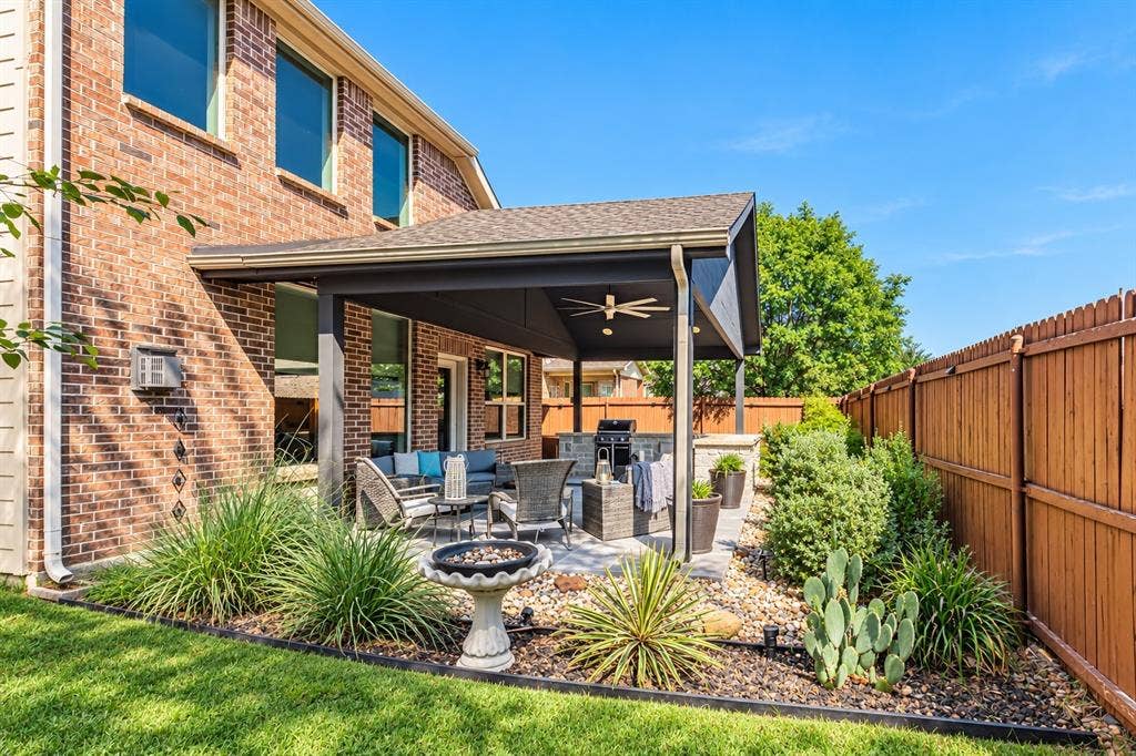 1704 Keswick Drive, McKinney, TX 75071 Covered patio with ceiling fan and integrated lighting overlooking a manicured lawn with ornamental grasses, desert plantings, and decorative stone hardscaping