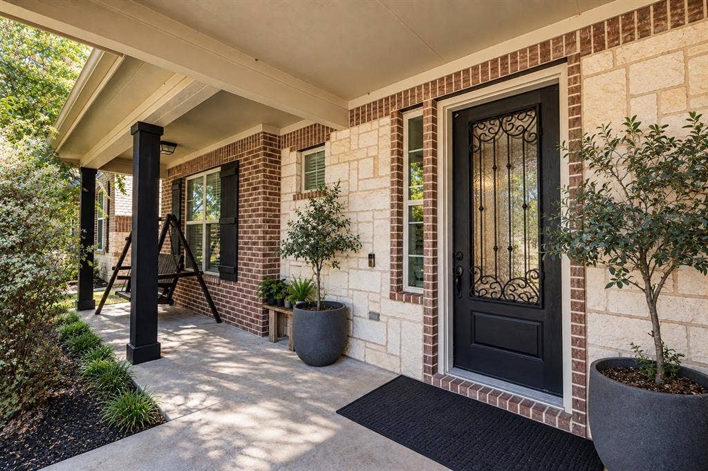 1704 Keswick Drive, McKinney, TX 75071 Covered front porch featuring a black decorative glass entry door, brick and stone exterior, and black-painted columns